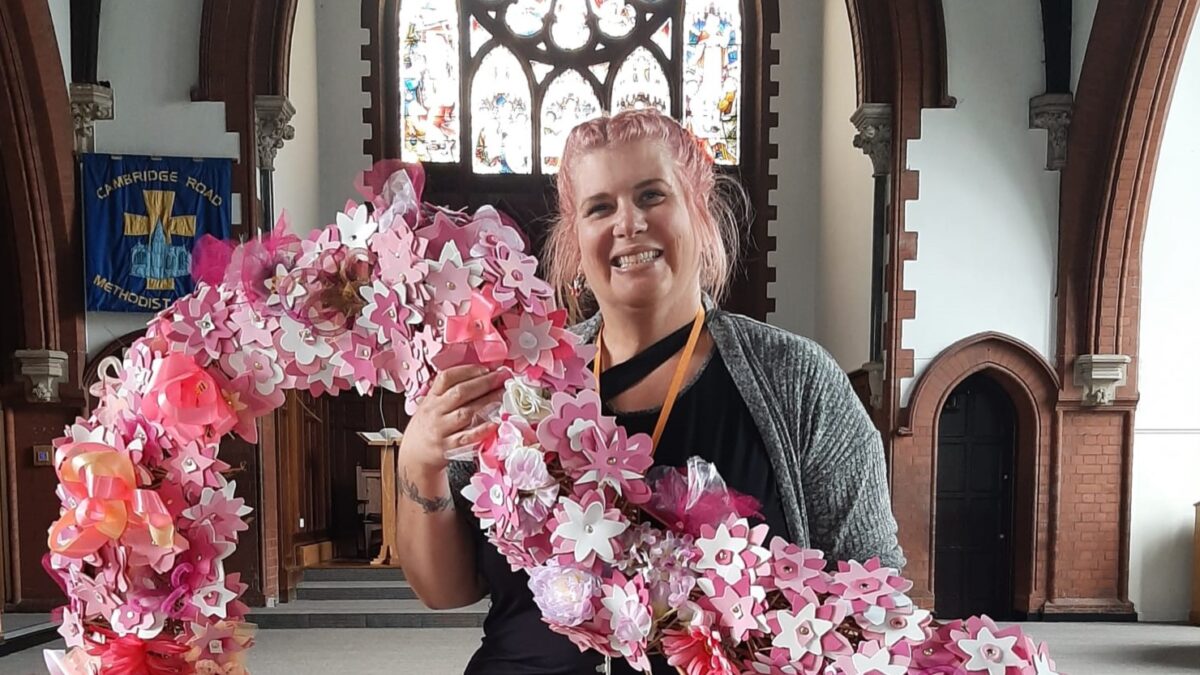 Smiling woman holds a big heart made from foam blossoms inside a large church